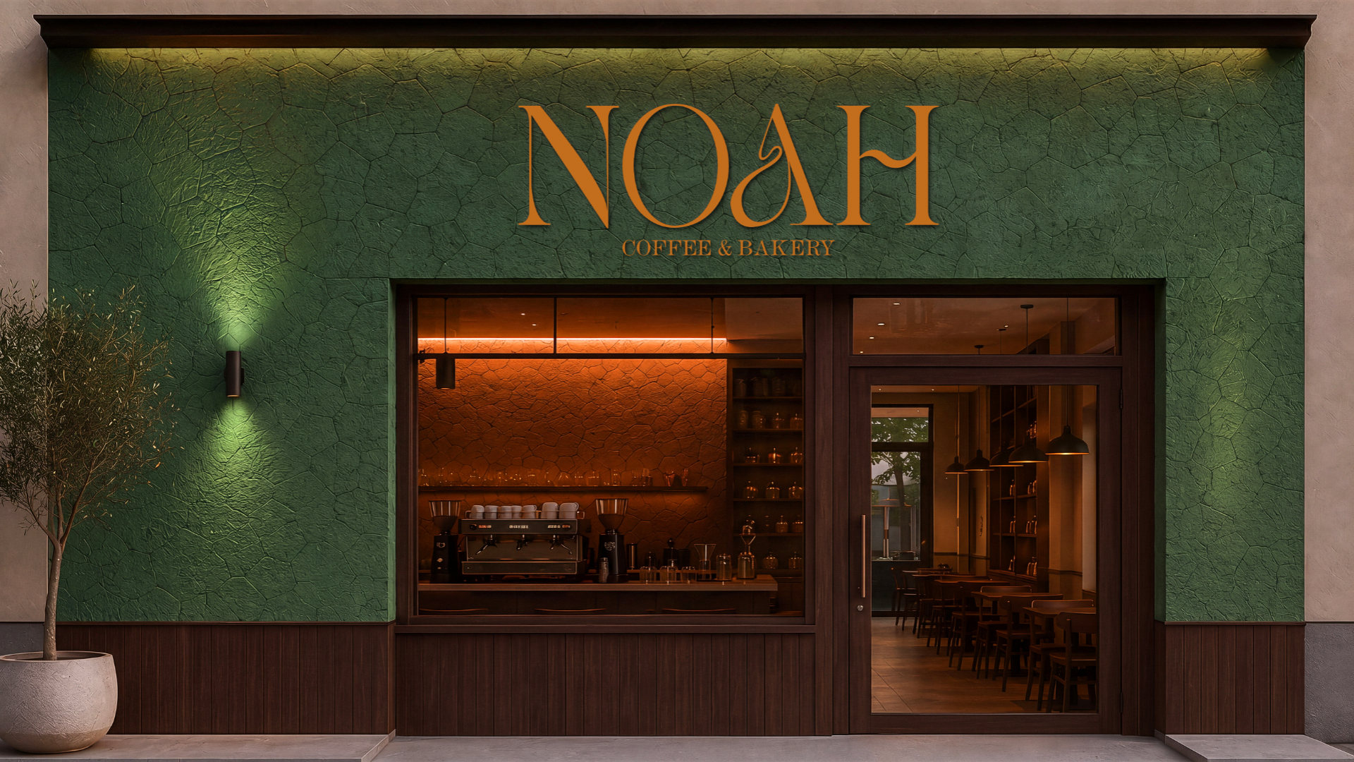 Fachada da NOAH em verde texturizado, com o logotipo em laranja acima da vitrine e o sal&atilde;o iluminado ao fundo.